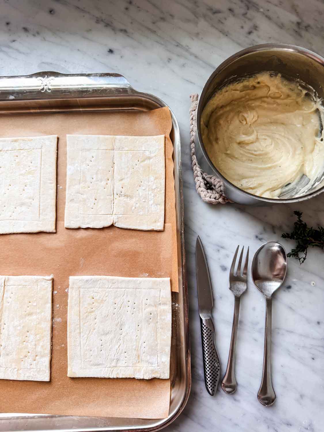 Puff pastry rectangles are placed on a parchment paper-lined baking sheet, and béchamel sauce is prepared in a small saucepan.