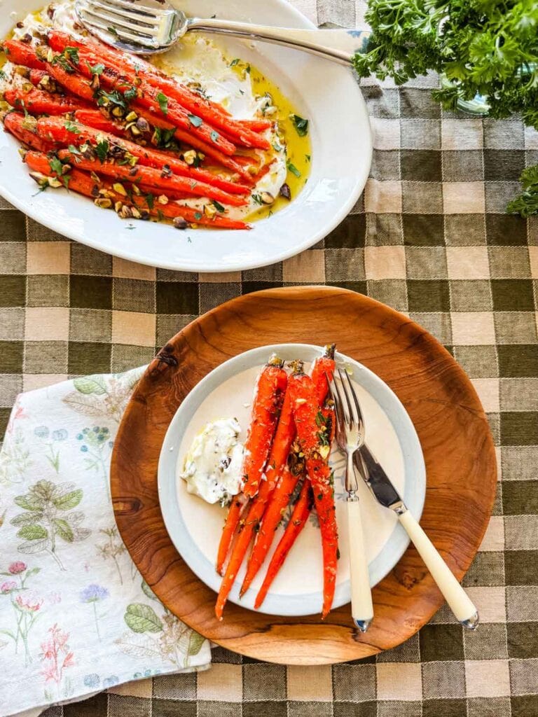 Apilco platter with roasted carrots sprinkled with fresh herbs and pistachios. Wood charger with plate, carrots, knife and fork.