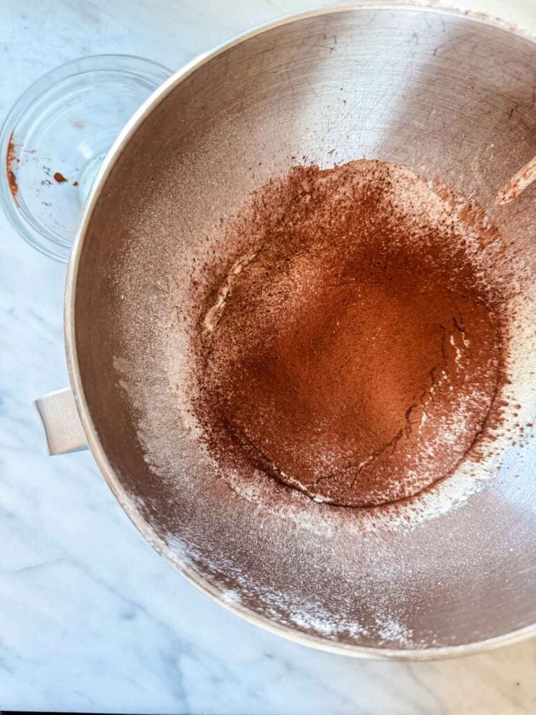 The dry ingredients for chocolate madeleines have been sifted into the wet ingredients in the bowl of a stand mixer.