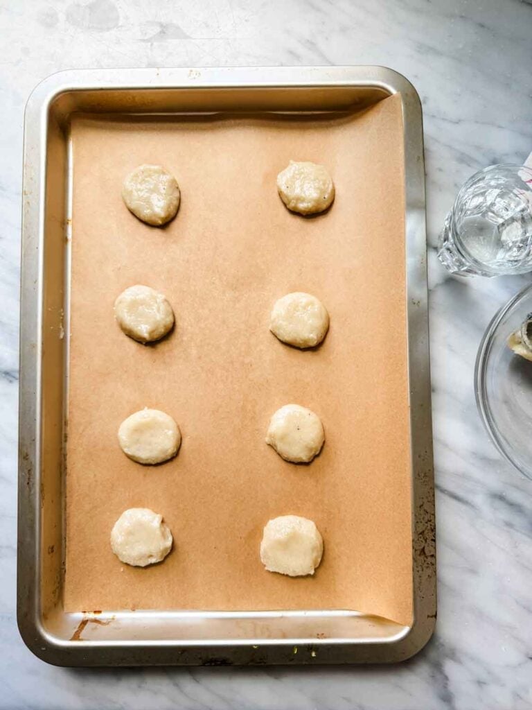 Macaron batter is scooped on the baking sheets and the tops are smoothed out using your finger tip dipped in water first.
