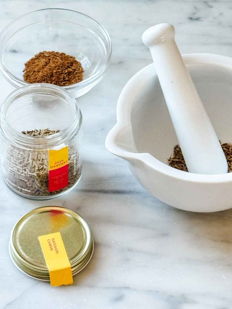 Mortar and pestle with cumin seeds, jar of cum seeds. dish of toasted cumin seeds.