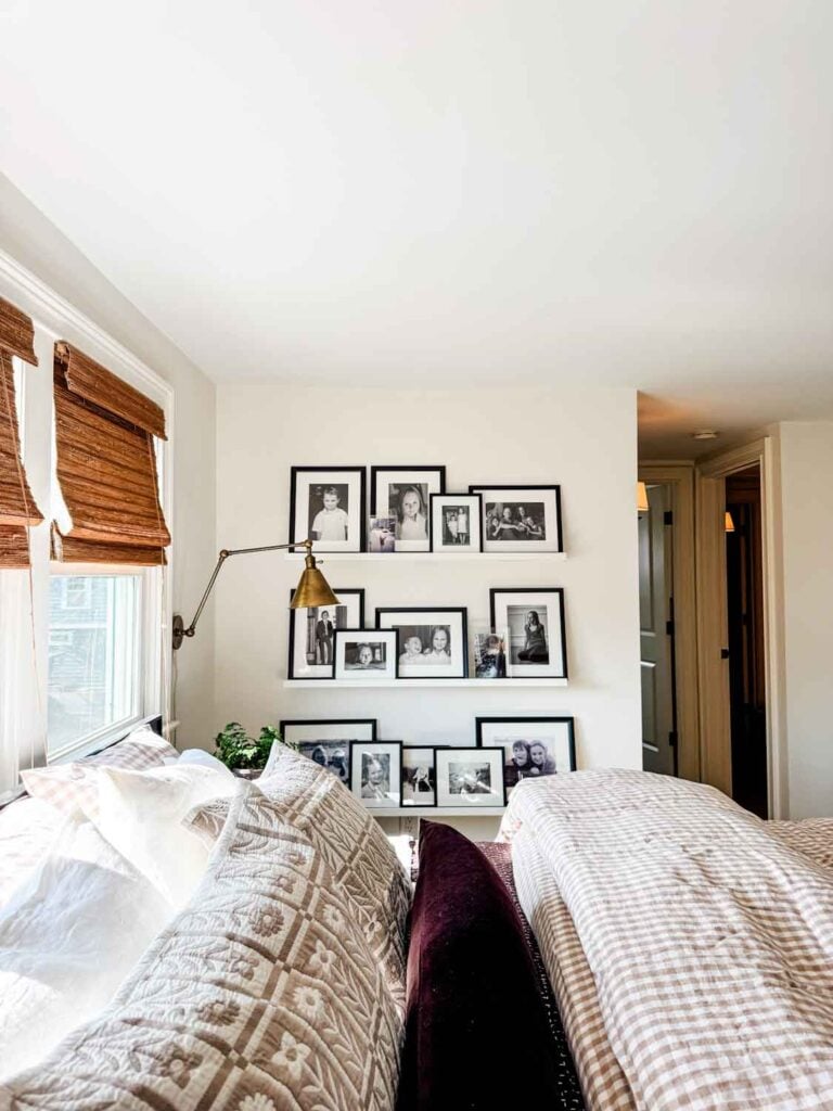 Ginham divet cover on bed, framed photos on photo ledges, woven wood blinds on windows.