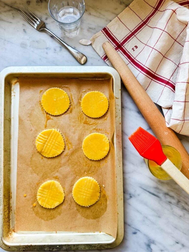 Using a pastry brush, the tops of the cookies are brushed with egg yolk to create a golden brown finish on the cookie tops.