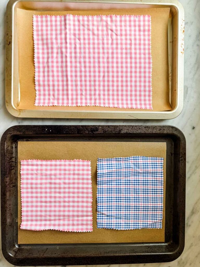 Fabric squares and rectangles are placed on parchment paper-lined baking sheets, ready for the beeswax application.