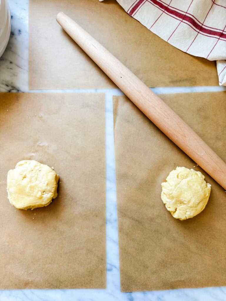 The dough is cut in half and placed between two sheets of parchment paper before it is rolled out.