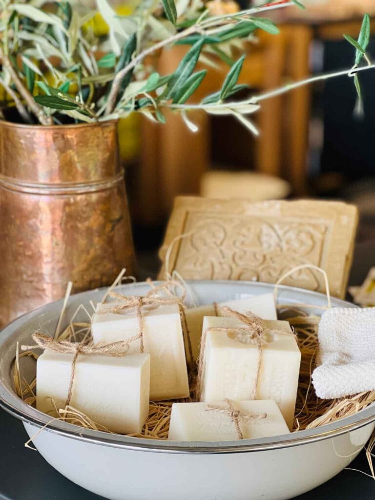 Cubes of rosemary scented soap are in a vintage bowl next to a copper vase full of fresh rosemary springs.