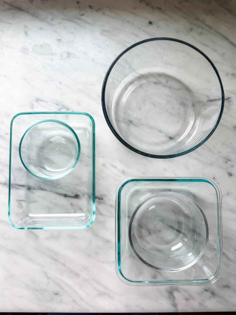 Glass food containers of different sizes and without lids are sitting on a kitchen counter.