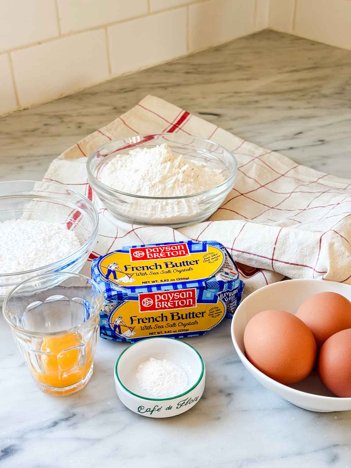 The ingredients for French sablés breton cookies are flour, powdered sugar, egg yolks, butter, and baking powder. All ingredients are sitting on the countertop ready for mixing.