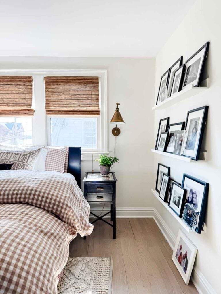 Black nightstand with brass sconce above, beside a bed woth gigham bedding.
