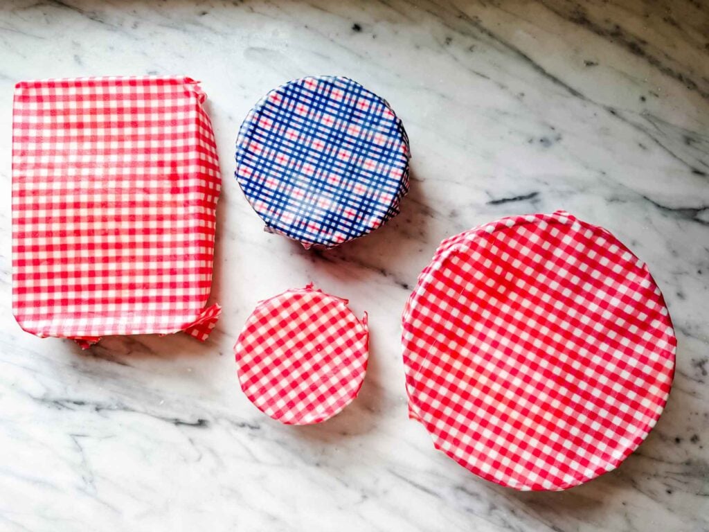 Different-sized food containers, on a kitchen counter, are covered with reusable beeswax wraps made from the fabric of old 100 percent cotton shirts.