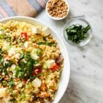Ina Garten's orzo with roasted vegetables is in a large white serving bowl next to toasted pine nuts and basil.
