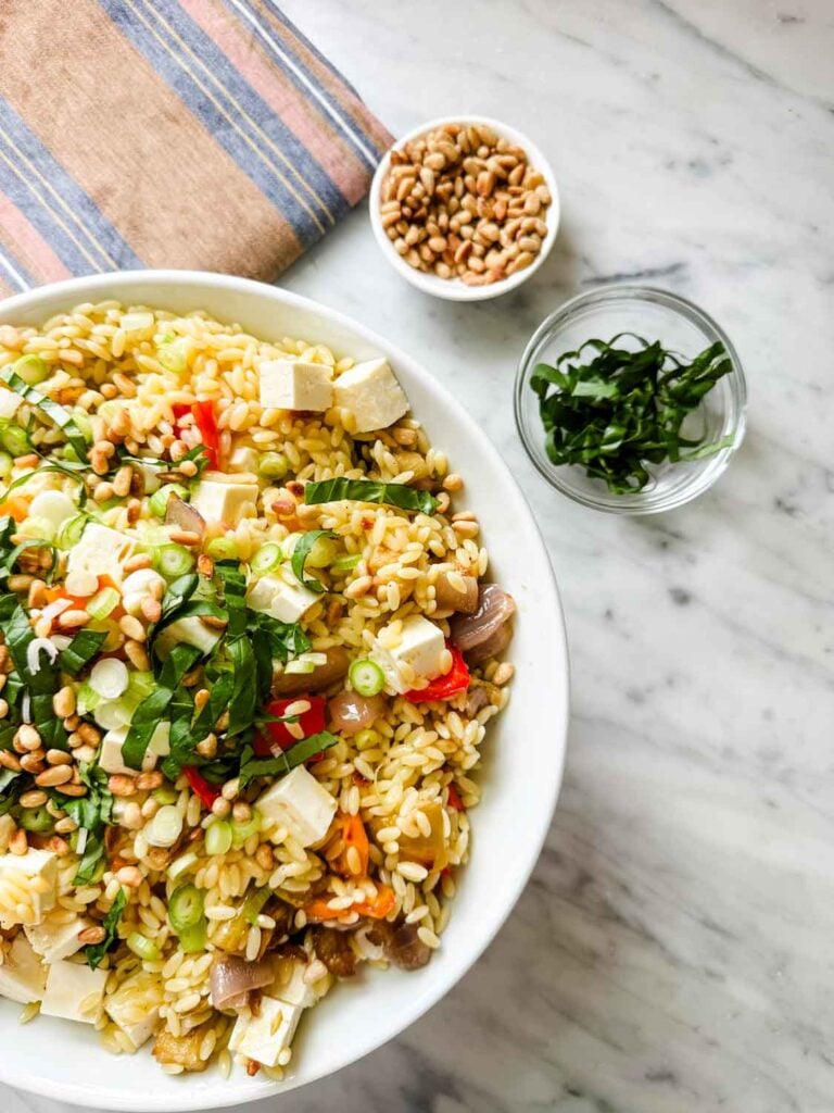 Ina Garten's orzo with roasted vegetables and feta cheese is ready to be topped with toasted pine nuts and basil.