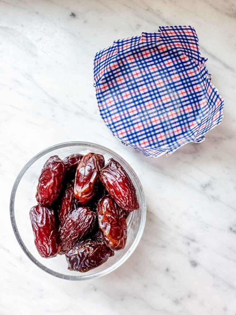 Dates are placed in a small, glass bowl, and a beeswax food wrap is used to cover the top when storing in the refrigerator.