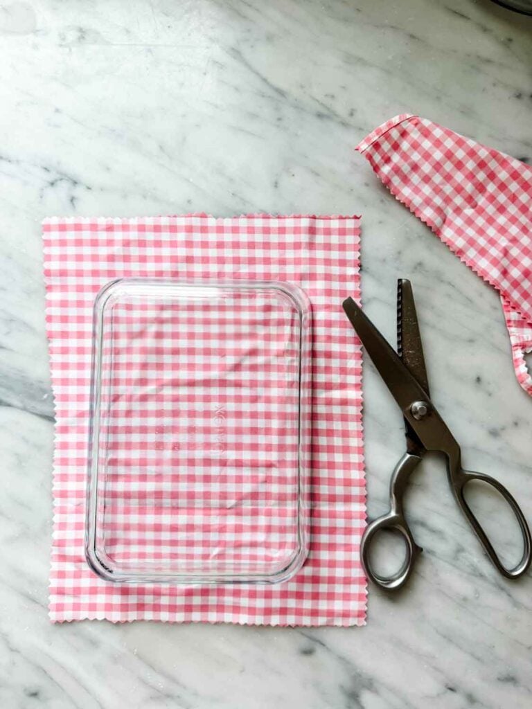 Fabric, cut from a shirt, is being measured to be used as a beeswax food wrap. Shears and scraps of fabric are off to the side.
