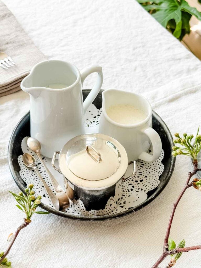 Pitchers, filled with cream, are served with stirring spoons on a round, metal platter.