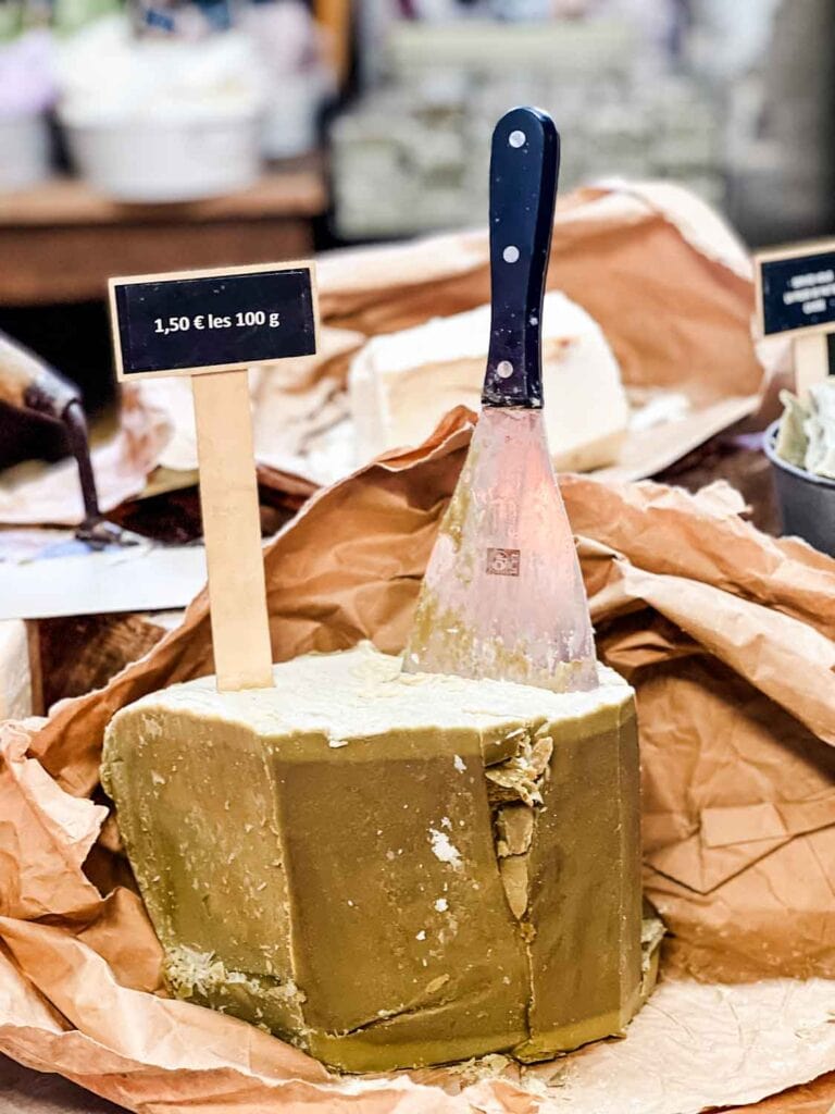 A block of soap that you can buy by weight sits on butcher paper and a cutting knife is stuck on the top of the soap block.