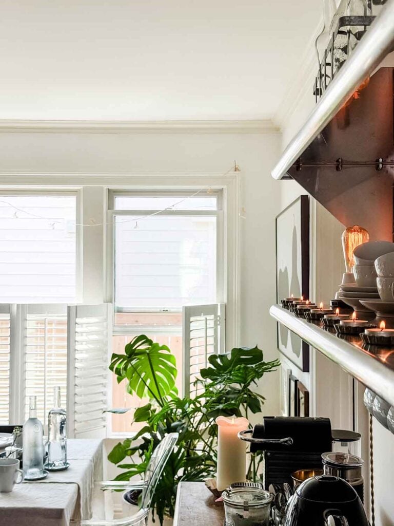 A candle is buring on a coffee bar with a brunch table in the background.