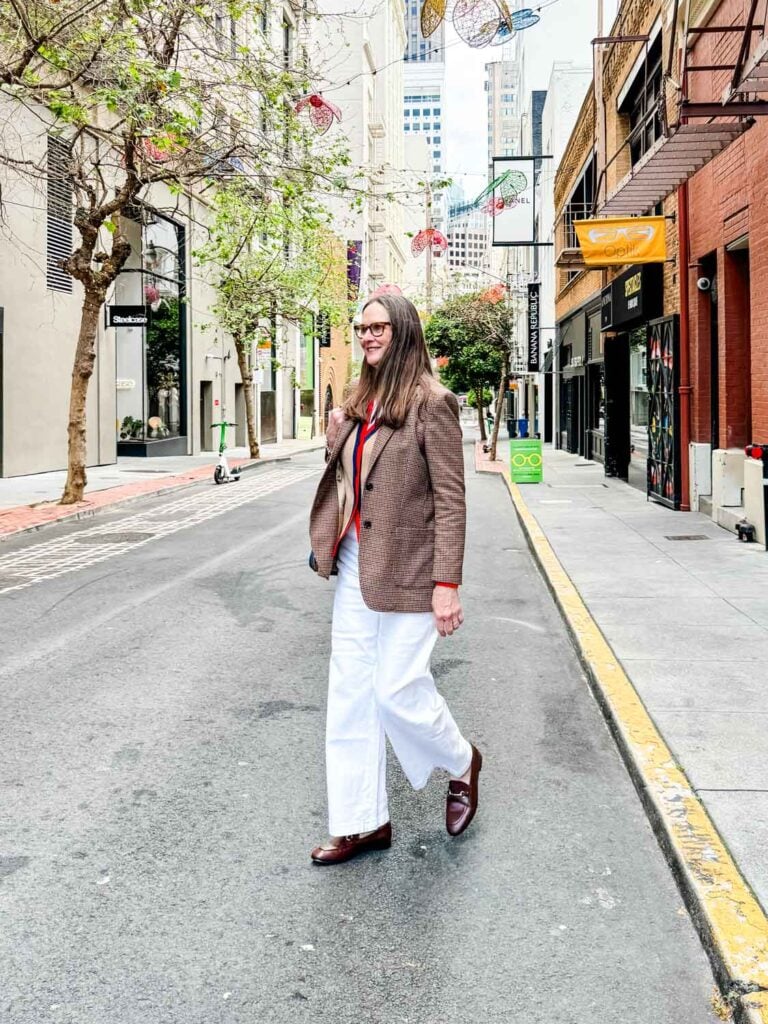 Woman walking wearing cardigan sweater, white jeans, Gucci loafers, white tank. 