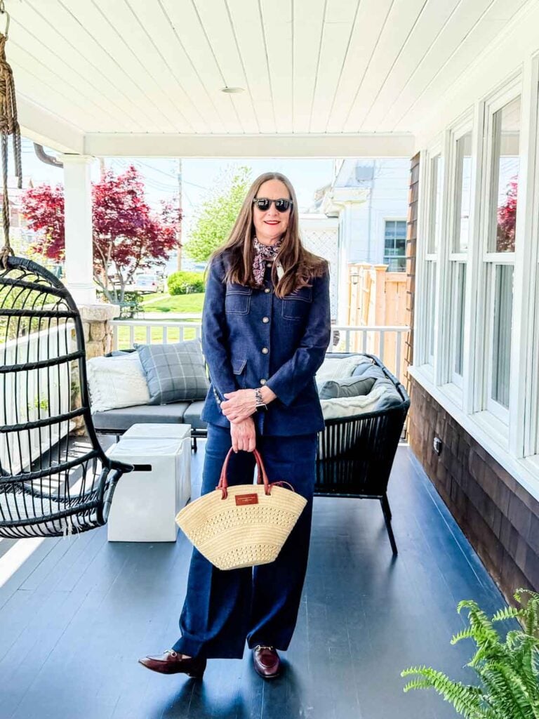Woman standing on porch in denim suit holding a basket bag.