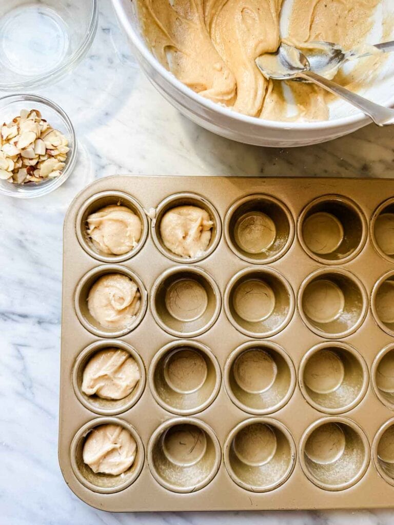 French tea cake batter is being poured into mini muffin tins. 