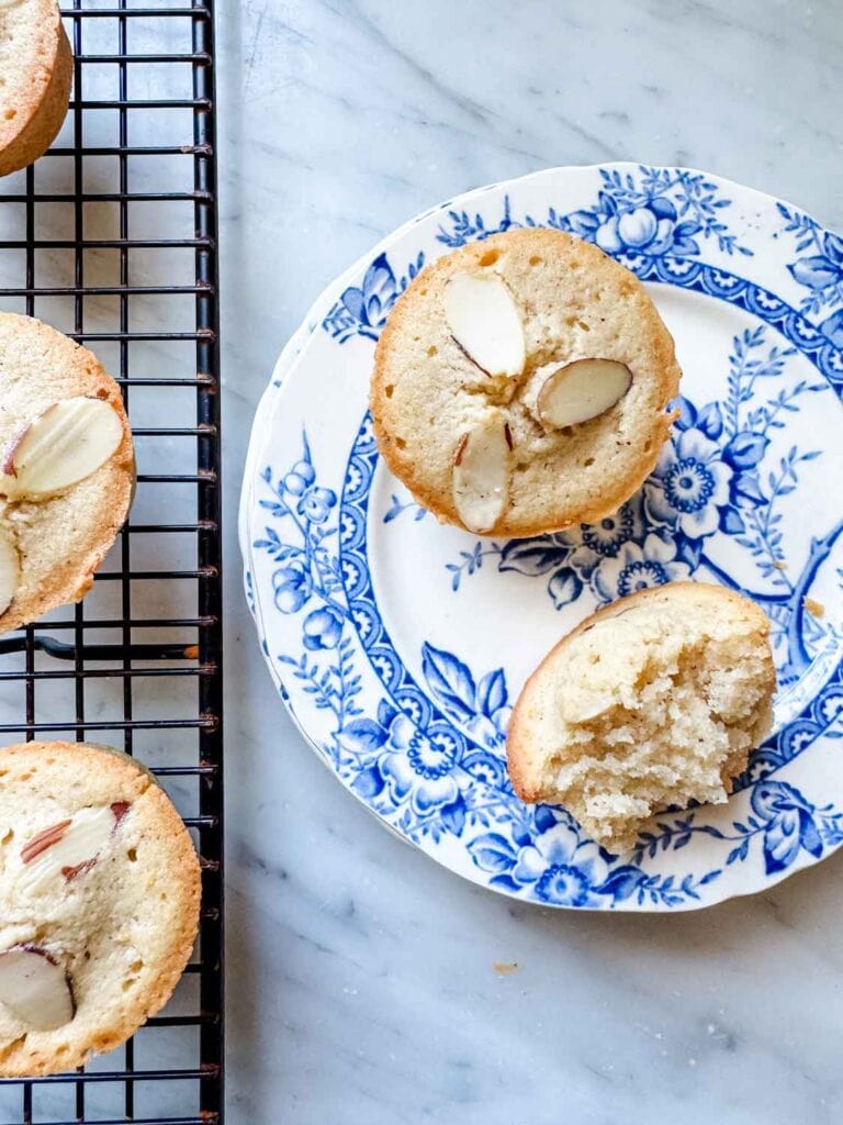 Classic French financier cakes are on a vintage plate. One is broken in half to show the cake-like inside.