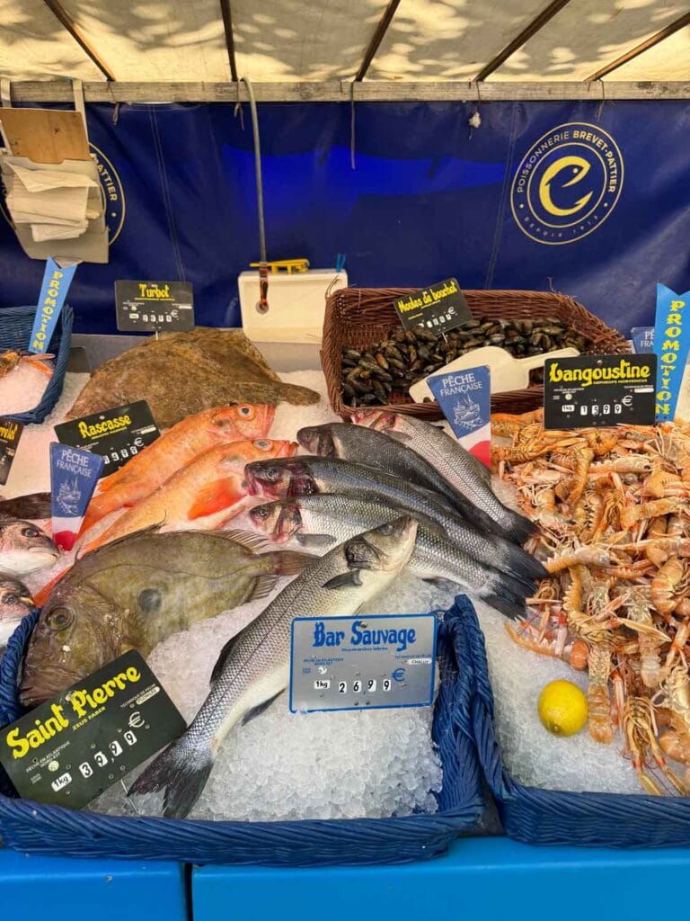 Fresh fish in small plastic tubs are on sale are in case at Marché Raspail.