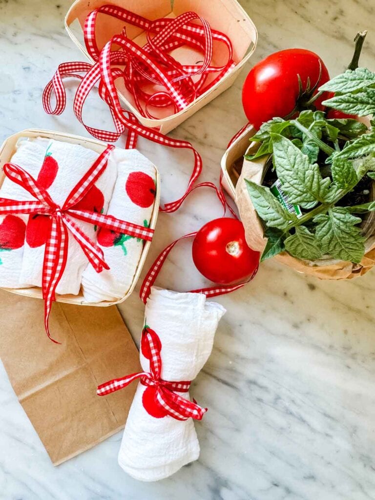 Tomato plant in a berry basket with a tea towel featuring a hand-painted tomato design, nd red and white gingham ribbon.