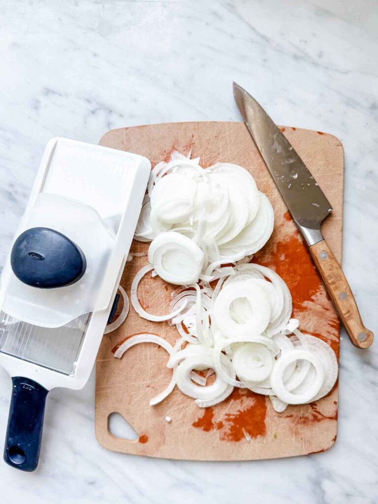 Mandolin, sliced onions, sharp knife on cutting board. 