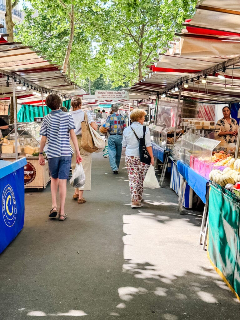 Shoppers with bags are walking through Marché Raspail on a weekday in Paris.