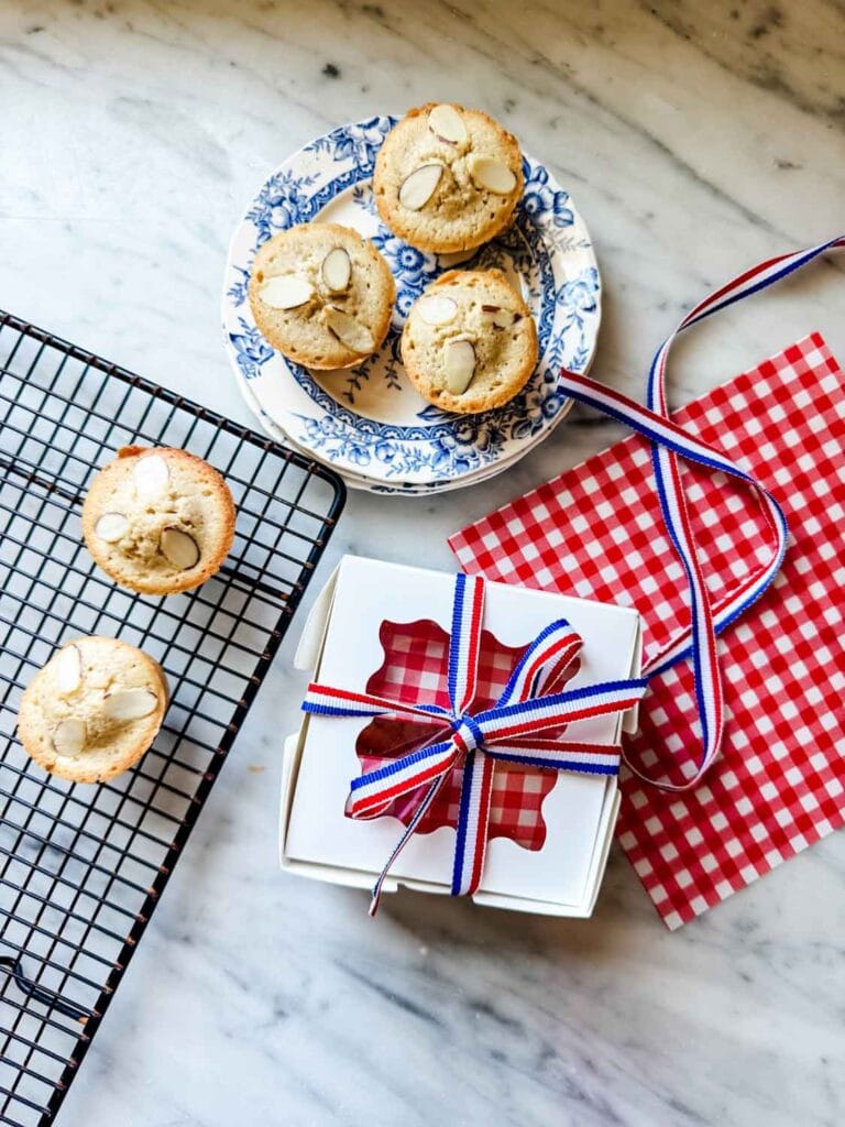 Classic French financier cakes are in a small, white pastry box wrapped with red, white, and blue French ribbon. 