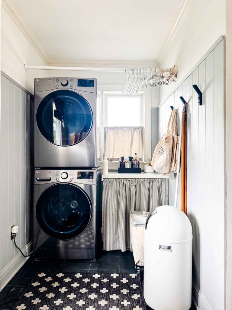 Wahser and dryer stacked with hooks, hangers on bar.