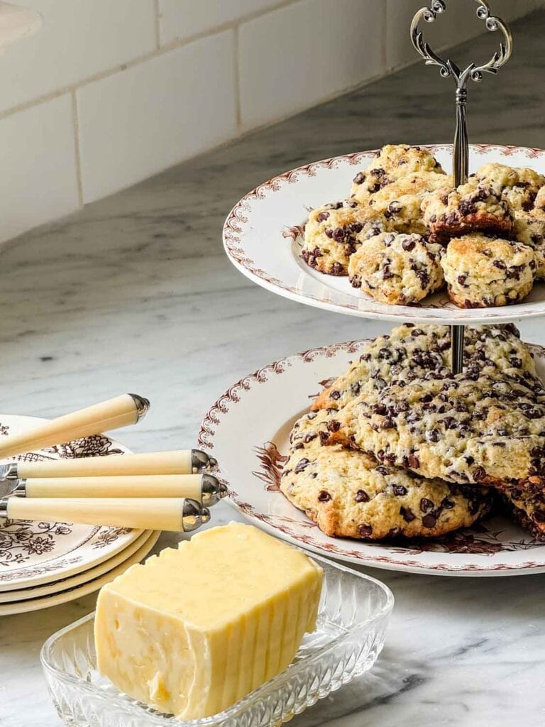 Tiered plates with scones, butter in glass dish, knife handles on small plates.