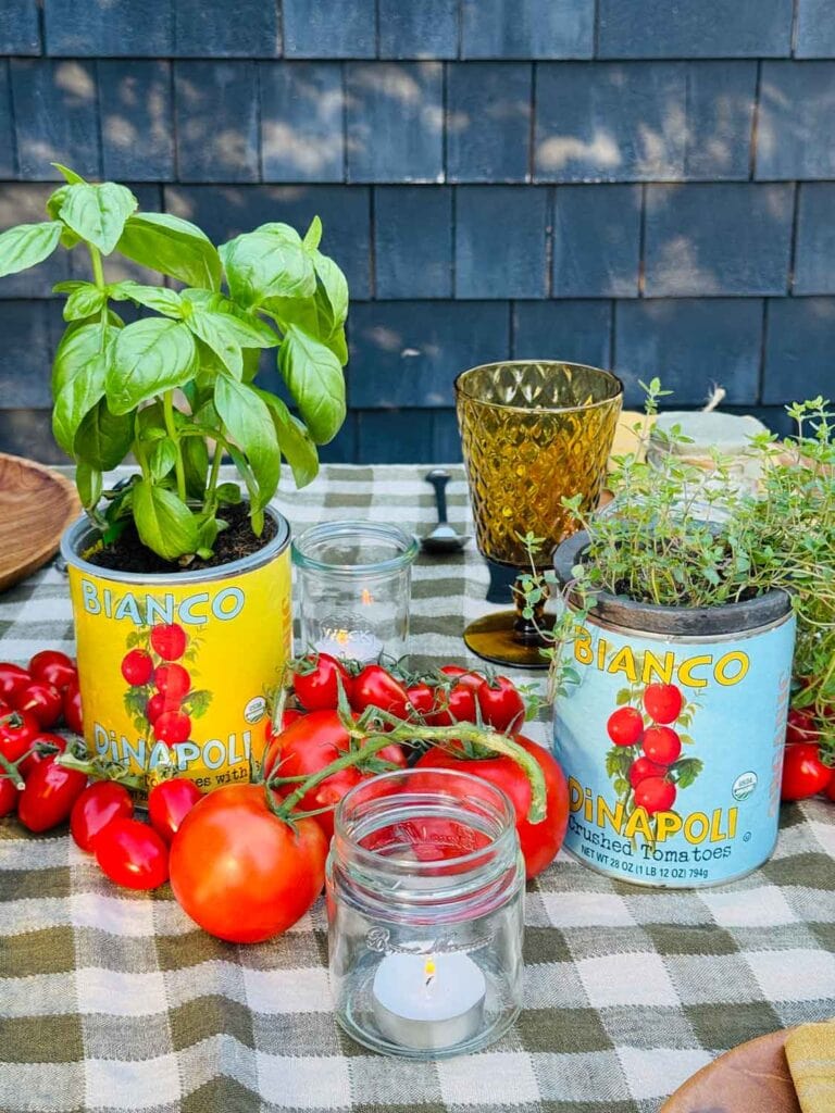 Bianco tin tomato cans with herbs, tomatoes, small jars with votices.