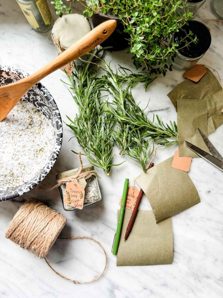 Jars of salt with small kraft colored tags, fresh rosemary, black lid and a rubberband on a marble counter.
