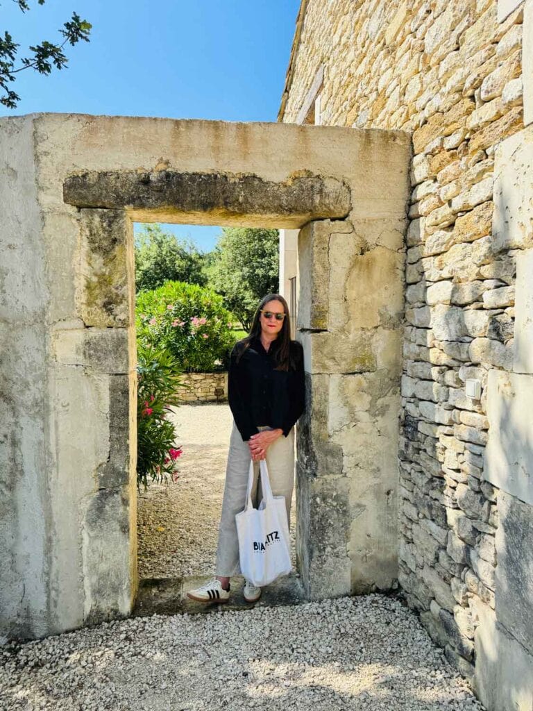 Woman wearing a black shirt and natural linen pants with a cream colored tote bag in Provence.
