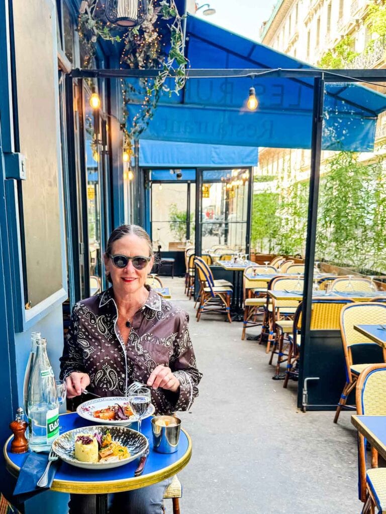 Woman wearing sunglasses dining at a bistro, sitting at a table on the patio.