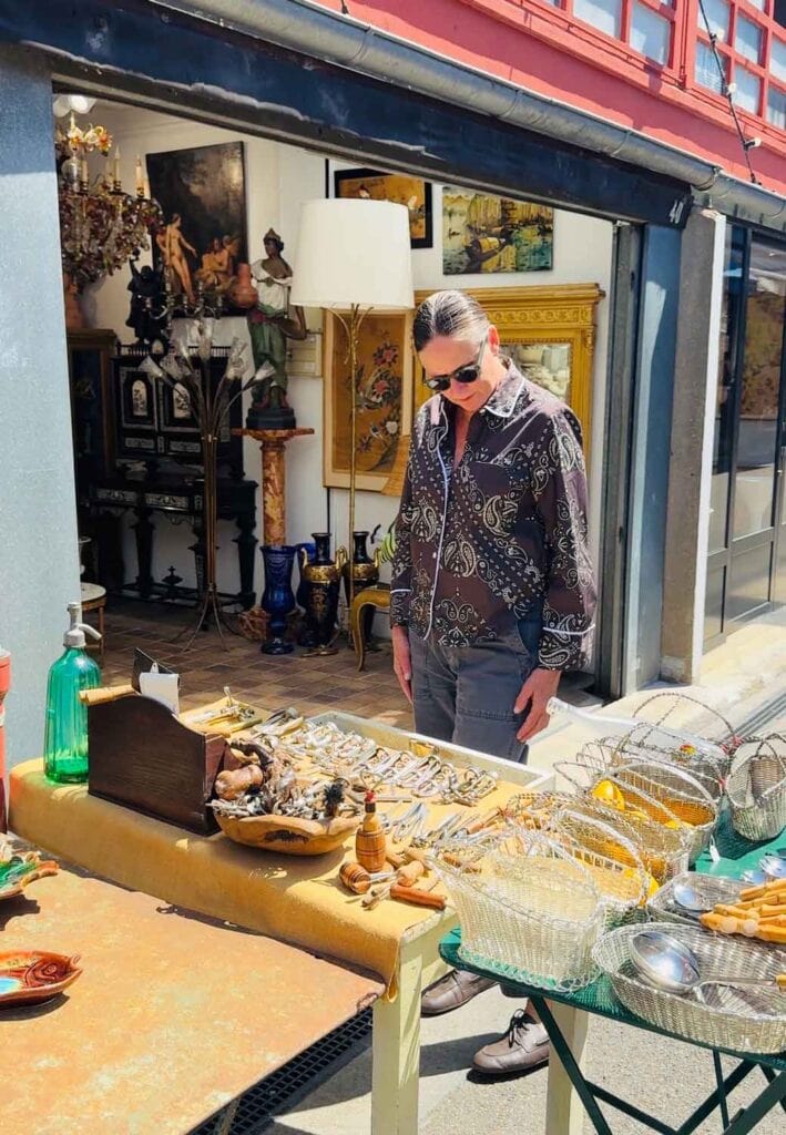 Woman wearing brown patterned shirt and sunglasses while shopping at a Paris flea market on a summer day.