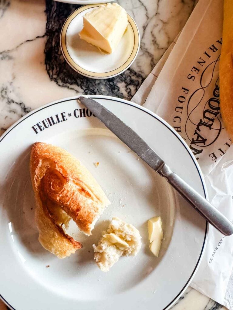 A torn piece of baguette is sitting on a plate with butter and a knife.