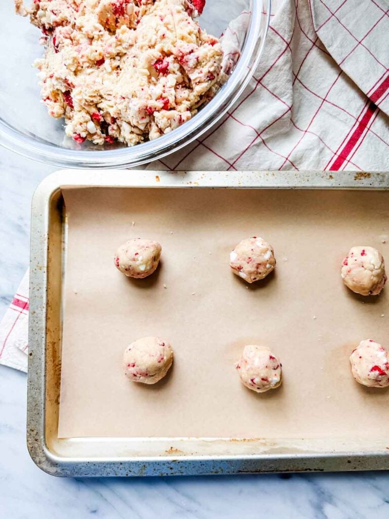 Cookie dough with freeze dried strawberries on parchment paper lined baking sheets.