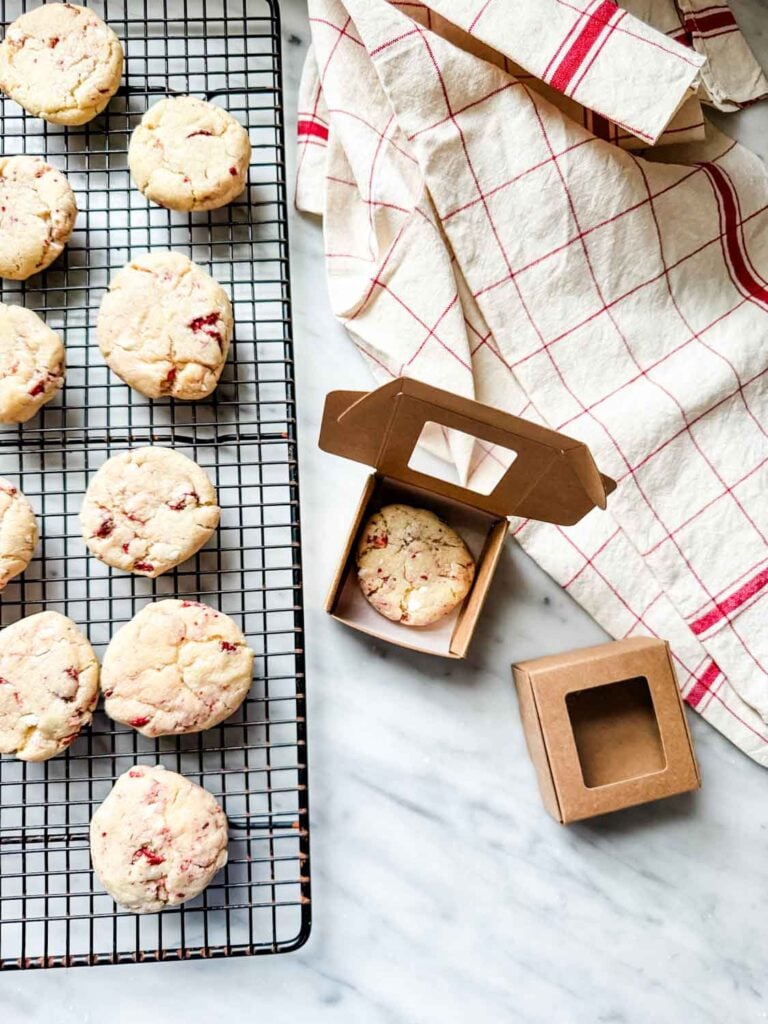 Strawberry cheesecake cookies on cooling rack and in tiny boxes made of kraft paper.