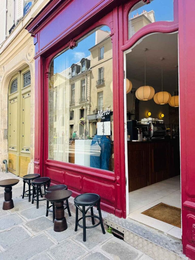 Coffee shop painted merlo red with small black stools on the sidewalk in Paris.