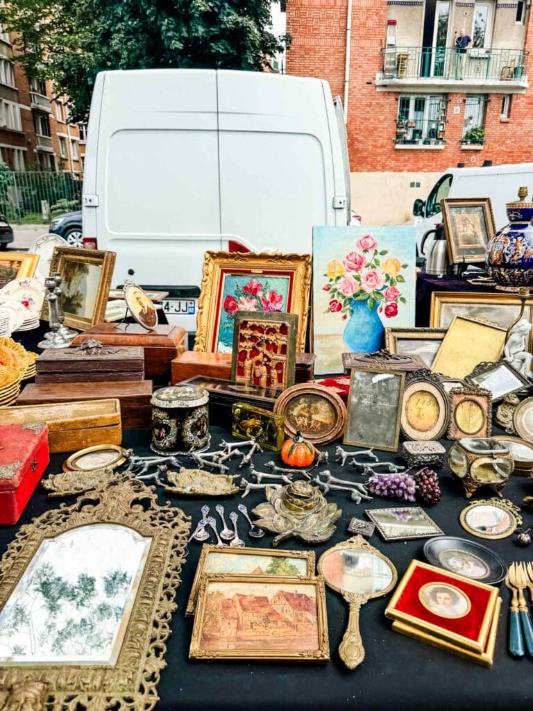 Old picture frames, hand mirrors, silver spoons, and other vintage products are on display tables at Portes de Vanves Flea Market in Paris.