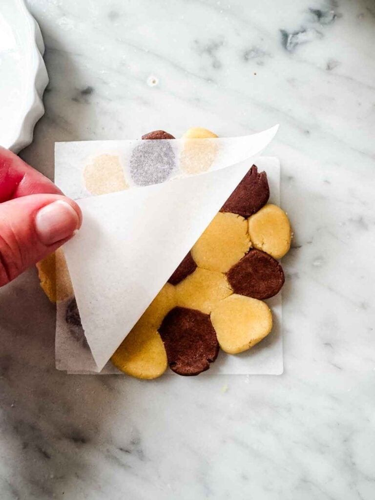 Vanilla and chocolate cookie dough, small dough balls, flattened, and lifting off the parchment paper.