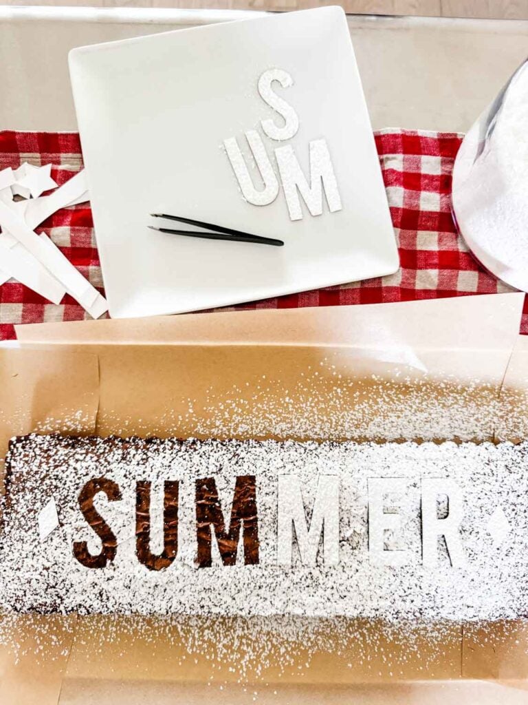 The word summer is spelled out on the top of this brownie which is resting on sheets of parchment paper.
