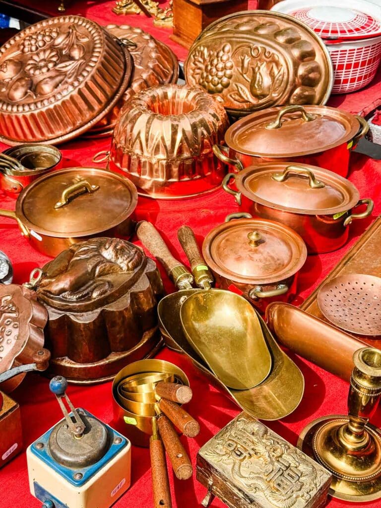 Vintage copper pots of all sizes and shapes are displayed on a red tablecloth on this large table.