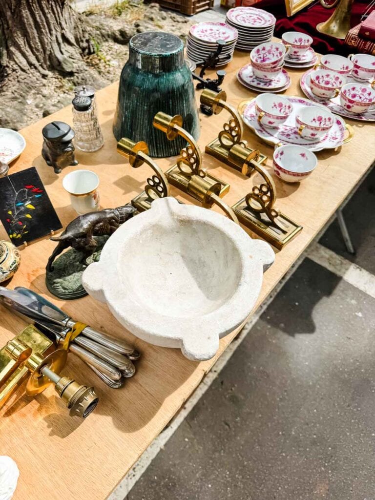 Vintage brass wall sconces, a large pestle, intage china, and may other items are displayed on this table.
