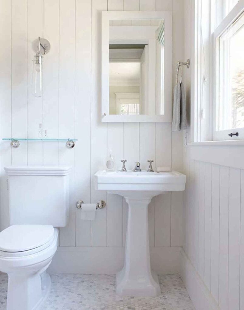 White pedestal sink. mirror, white paneled walls.
