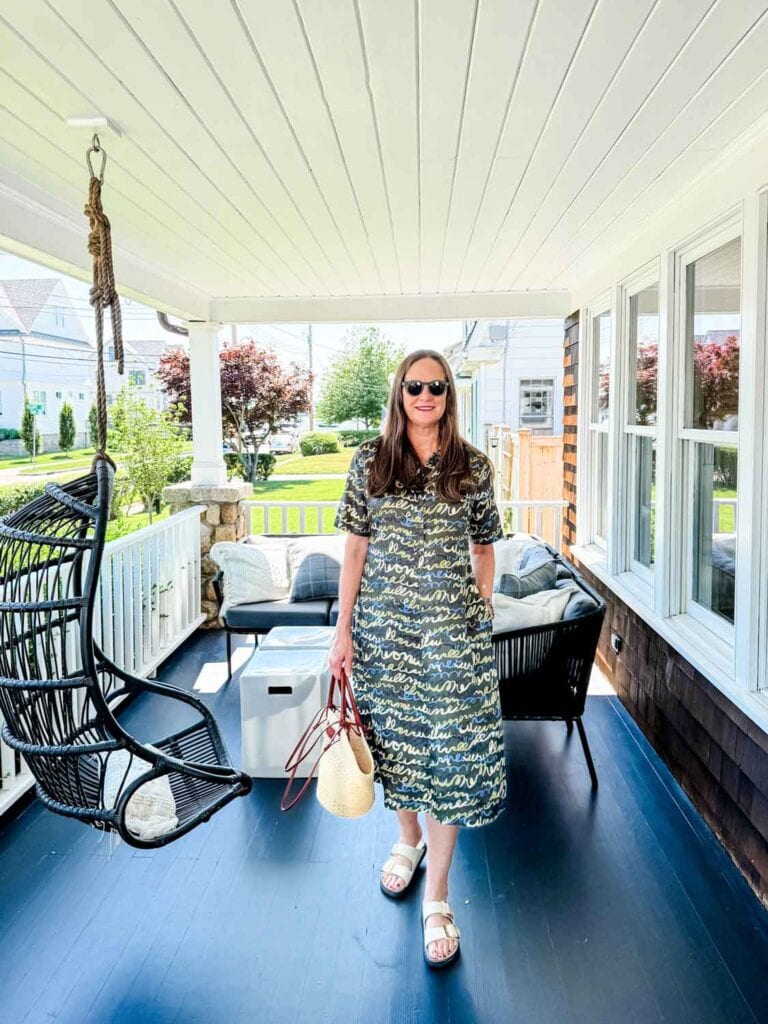 Annie Diamond wearing a shirt dress, Birkenstocks, basaket bag on a porch.