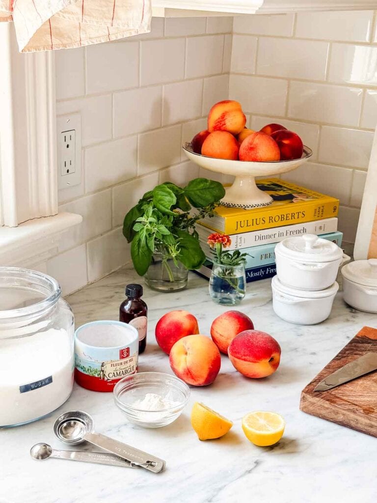 Peaches, herbs, marigold, white Staub cocottes, lemon, salt, sugar, cookbooks, measuring spoons. 