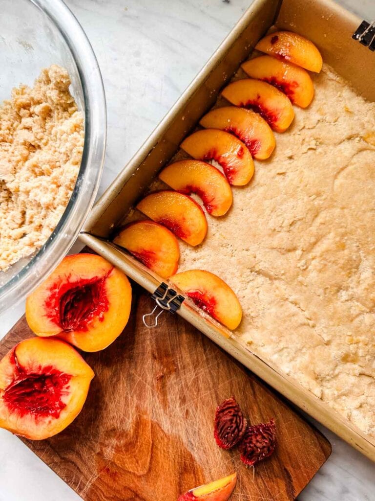 The shortbread crust is being lined with sliced peaches.